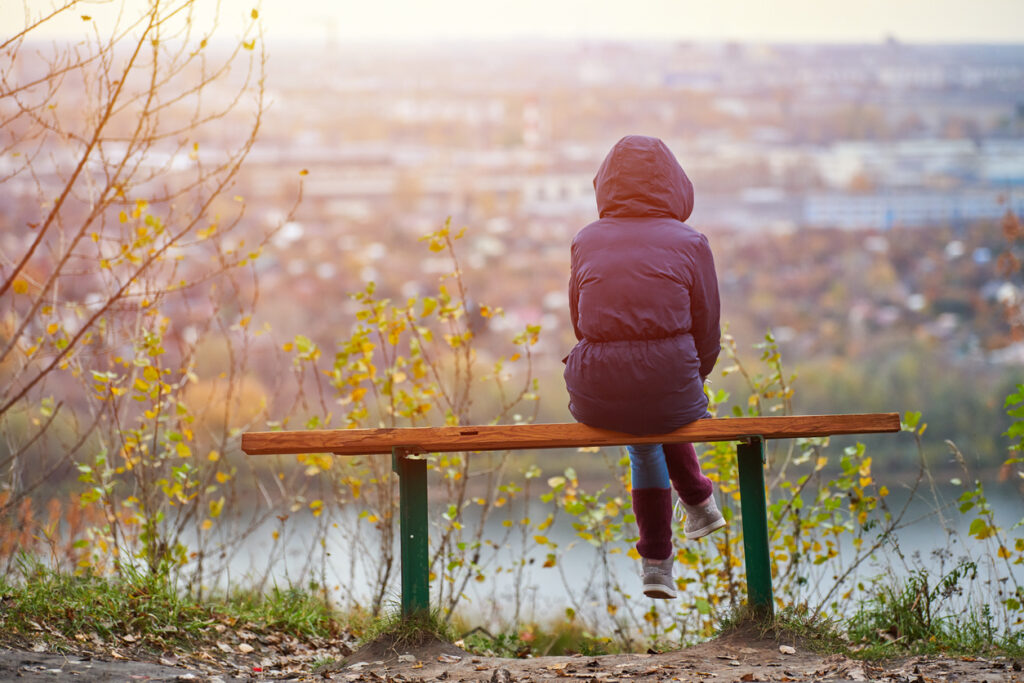 Photo of woman sitting on bench looking out over river.